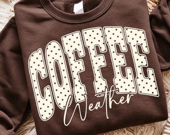 May include: A dark brown crewneck sweatshirt featuring the word COFFEE in large, cream-colored, polka-dotted block letters. Below the word COFFEE, the word Weather is printed in a white, cursive script font across the center of the chest.