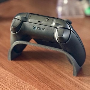 Op de afbeelding: Een zwarte Xbox-controller met een oplaadpoort aan de achterkant. De controller staat op een oplaadstandaard.