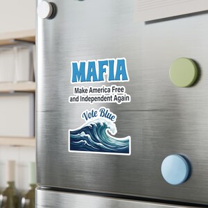 May include: A rectangular sticker featuring the blue text MAFIA above the black text Make America Free and Independent Again, positioned above a second sticker showing a blue ocean wave with the white text Vote Blue written in cursive.