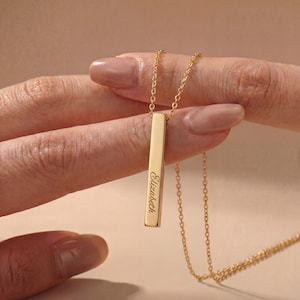 Peut inclure: Un collier pendentif barre verticale doré avec le prénom Elizabeth gravé en écriture cursive. Le pendentif est suspendu à une fine chaîne dorée assortie, présentant une finition métallique polie et un design rectangulaire élancé.