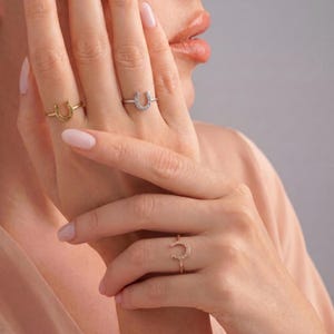 Può includere: Tre anelli sottili in metallo, ognuno caratterizzato da un piccolo ciondolo a forma di ferro di cavallo. Un anello è color oro, uno color argento e uno color oro rosa. Ogni anello presenta un design semplice e sottile.