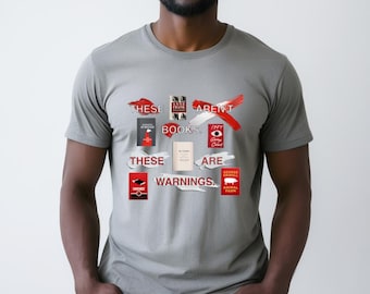 May include: A gray t-shirt with a red graphic that says "These aren't books, these are warnings." The graphic features the covers of several books, including "The Handmaid's Tale", "Anne Frank's Diary", "1984", "Animal Farm", and "The Diary of a Young Girl".