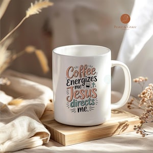 Puede incluir: Taza de café de cerámica blanca con el texto "Coffee energizes me, Jesus directs me" en varios colores. La taza tiene un asa curva y está sobre un bloque de madera.