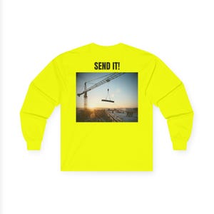 May include: Bright yellow long-sleeve shirt with the text "SEND IT!" above a rectangular image. The image depicts a construction crane lifting a beam at sunset. The shirt is a vibrant, eye-catching color.