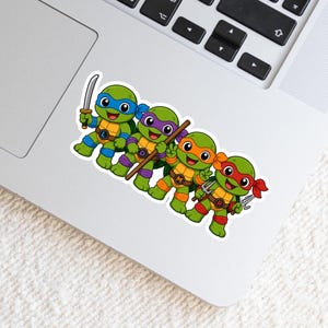 May include: A vinyl sticker featuring four cartoon turtles with green skin and tan shells. Each turtle wears a colored mask and matching wrist and ankle bands in blue, purple, orange, or red. They hold weapons including a sword, staff, and sai.