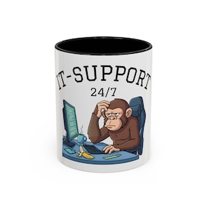 Könnte beinhalten: Weißer Keramikbecher mit schwarzem Innenraum und dem Aufdruck "IT-SUPPORT 24/7". Der Becher zeigt eine Cartoon-Illustration eines Affen, der an einem Schreibtisch sitzt und gestresst aussieht. Eine Banane und eine Tasse Kaffee sind ebenfalls auf dem Schreibtisch.