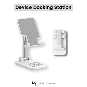 May include: A white and silver device docking station with a gray textured surface for a phone or tablet. The base has a custom logo. The text "Device Docking Station" is at the top.