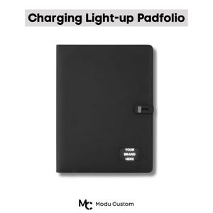 Può includere: Padfolio nero ricaricabile e illuminato con chiusura a fibbia. Il testo "Charging Light-up Padfolio" è in alto. In basso a destra c'è un piccolo quadrato con la scritta "YOUR BRAND HERE".