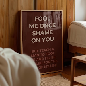 Puede incluir: Una impresión enmarcada con un fondo burdeos y texto blanco que dice "Fool me once shame on you, but teach a man to fool me and I'll be fooled for the rest of my life."