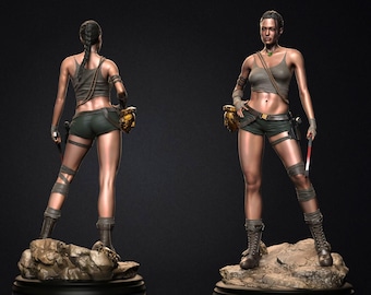May include: A female action figure with brown hair, wearing a green and brown outfit, holding a gold-coloured weapon in each hand. The figure is standing on a rocky base.