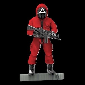 Może przedstawiać: Czerwona postać w kapturze z trójkątną maską trzyma czarny karabin. Postać stoi na szarej platformie z czarnym logo.