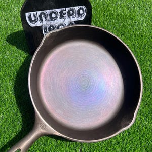 May include: A 10 inch cast iron skillet with a rainbow iridescent finish. The skillet is sitting on a green grassy surface.