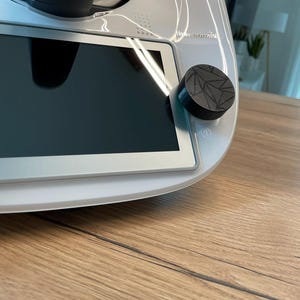 Könnte beinhalten: Ein weißes Küchengerät mit einem schwarzen Drehknopf und einem digitalen Bildschirm. Das Gerät steht auf einer Holztheke.