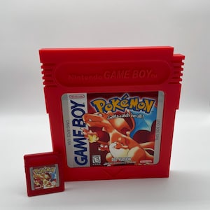 Könnte beinhalten: Eine rote Game Boy Color-Spielkassette mit einem roten Plastikgehäuse. Die Kassette ist für das Spiel Pokemon Red Version. Der Text auf der Kassette lautet "Gotta catch 'em all!" und "Red Version".