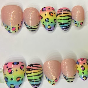 Op de afbeelding: Een set van tien kunstnagels met verschillende ontwerpen. Sommige nagels hebben een roze glitterbasis met een kleurrijke luipaardprint tip. Andere hebben een regenboog zebra streep ontwerp. De nagels zijn ovaal van vorm.