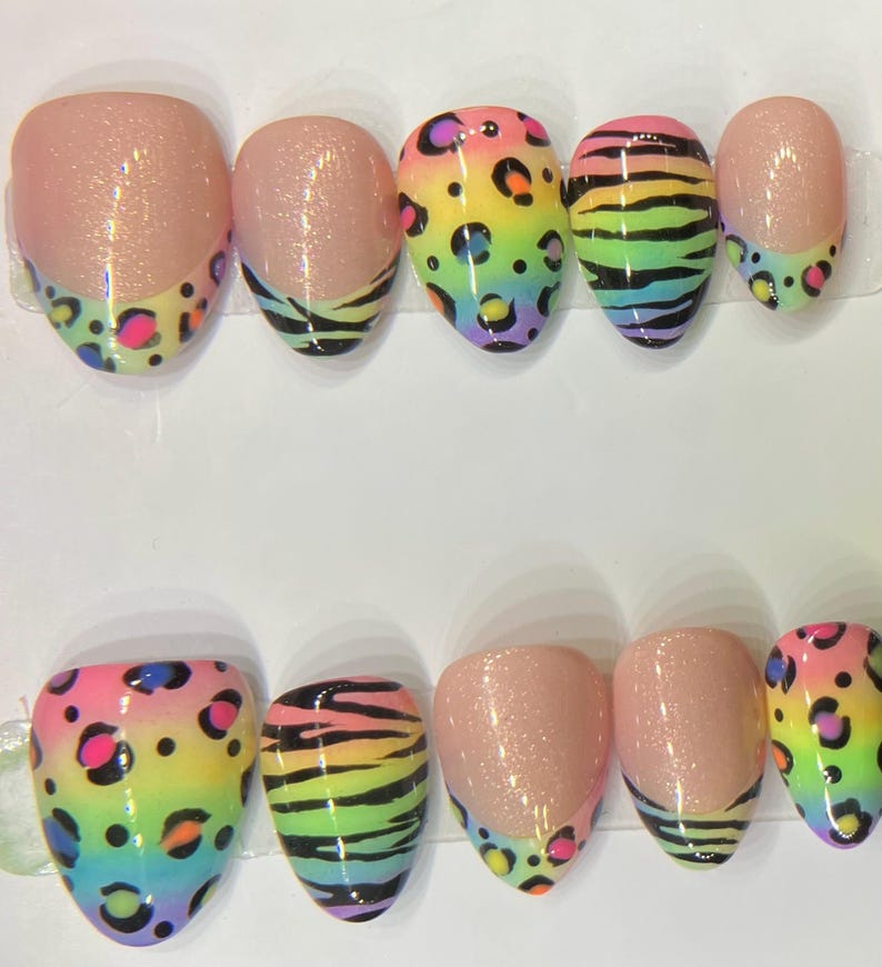 Op de afbeelding: Een set van tien kunstnagels met verschillende ontwerpen. Sommige nagels hebben een roze glitterbasis met een kleurrijke luipaardprint tip. Andere hebben een regenboog zebra streep ontwerp. De nagels zijn ovaal van vorm.