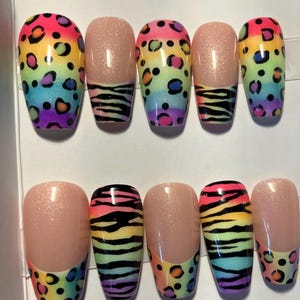 Op de afbeelding: Een set van tien kunstnagels met een regenboog luipaardprint ontwerp. Sommige nagels hebben een nude basis met een zebra streep patroon. De nagels zijn ovaal van vorm en hebben een glanzende afwerking, perfect voor een gedurfde en kleurrijke manicure.