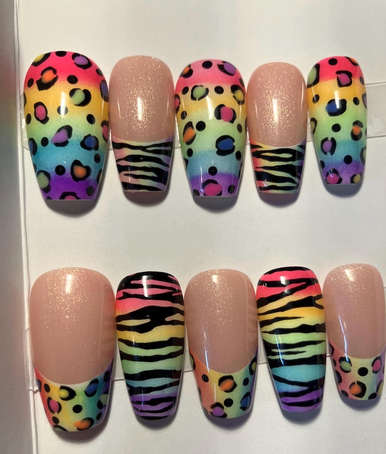 Op de afbeelding: Een set van tien kunstnagels met een regenboog luipaardprint ontwerp. Sommige nagels hebben een nude basis met een zebra streep patroon. De nagels zijn ovaal van vorm en hebben een glanzende afwerking, perfect voor een gedurfde en kleurrijke manicure.