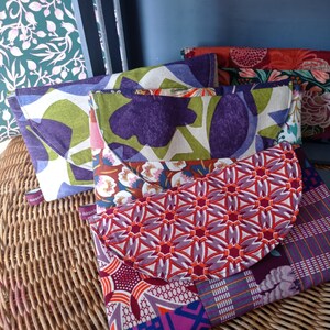 Peut inclure: Plusieurs pochettes en tissu colorées avec fermetures à rabat. Les pochettes présentent divers motifs, notamment floraux et géométriques, dans des tons de violet, vert, rouge et bleu. Chaque pochette porte une petite étiquette "Réséda".