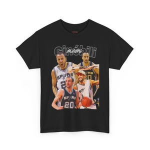 May include: Black t-shirt featuring a collage of images of a basketball player, with the name "Ginobili" printed above the images in white. The player is wearing a Spurs jersey in multiple images. The shirt is a crew neck.