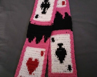 May include: A pink and black crocheted scarf with a design of playing cards. The scarf features a heart, spade, and diamond.