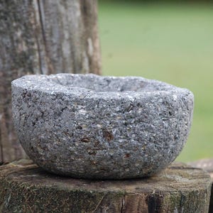 May include: A gray stone bowl with a rough, textured surface. The bowl is sitting on a wooden surface.