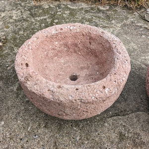 May include: Two pink terracotta pots with a rough, textured surface. The pots are round and have a drainage hole at the bottom.