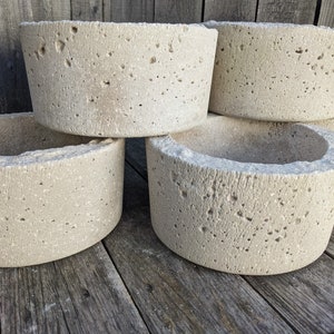 May include: Four concrete planters stacked on top of each other. The planters are a light beige color and have a rough, textured surface.
