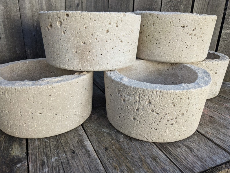 May include: Four concrete planters stacked on top of each other. The planters are a light beige color and have a rough, textured surface.