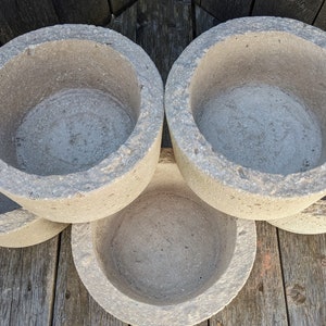 May include: Four gray concrete planters with a rough texture and rounded edges. The planters are stacked on top of each other.