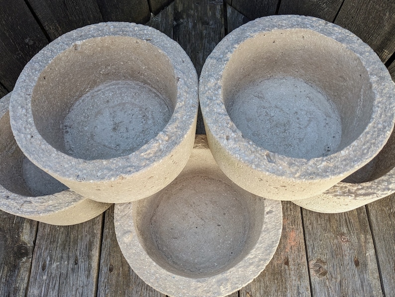 May include: Four gray concrete planters with a rough texture and rounded edges. The planters are stacked on top of each other.