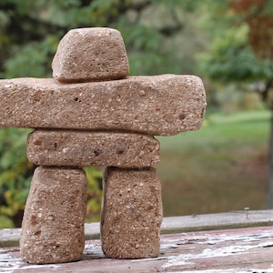 May include: A brown stone inukshuk sculpture, a traditional symbol of the Inuit people, is made of stacked rocks. The sculpture is on a wooden surface.