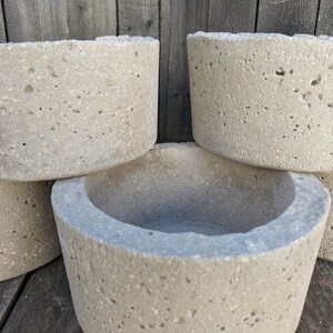May include: Four round concrete planters with a rough, textured surface. The planters are stacked on top of each other.