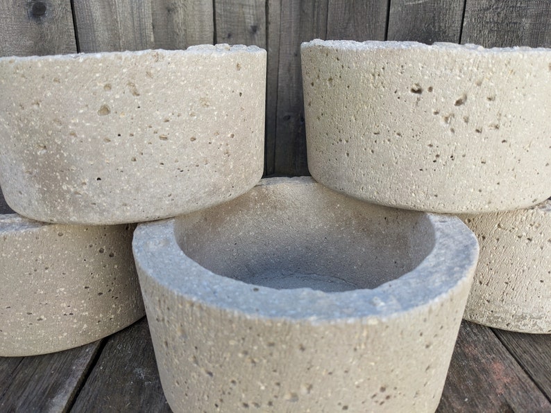 May include: Four round concrete planters with a rough, textured surface. The planters are stacked on top of each other.