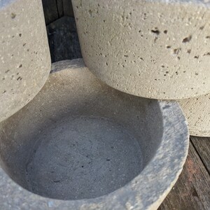 May include: A set of four gray concrete planters, one of which is a bowl with a smooth, rounded interior. The planters are stacked on top of each other, with the bowl on top.