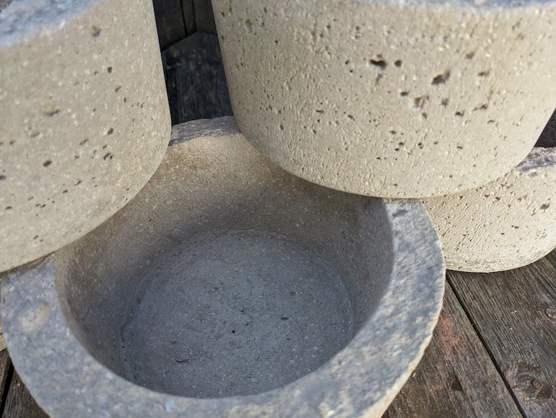 May include: A set of four gray concrete planters, one of which is a bowl with a smooth, rounded interior. The planters are stacked on top of each other, with the bowl on top.