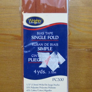 Op de afbeelding: Een pakket Wrights biaisband in de kleur specerij. De verpakking heeft de tekst "BIAS TAPE SINGLE FOLD" en "4 yds. 1/2" (13mm) breed". De verpakking ligt op een houten oppervlak.