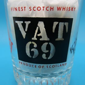Może przedstawiać: Przezroczysty szklany kubek z napisem "FINEST SCOTCH WHISKY" i "VAT 69 PRODUCE OF SCOTLAND". Szklanka jest wypełniona białym papierem i stoi na niebieskim tle.