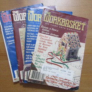 May include: Four copies of "The Workbasket" magazine, a home arts magazine. The front cover of the magazine features a gingerbread house with colourful candies and frosting. The magazine title is in red and yellow letters. The text "Create a Fancy Edible Cookie Cottage" is printed in black letters.