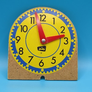 May include: A yellow and blue wooden clock with movable hands. The clock face has numbers 1 through 12 and the text "by Judy".
