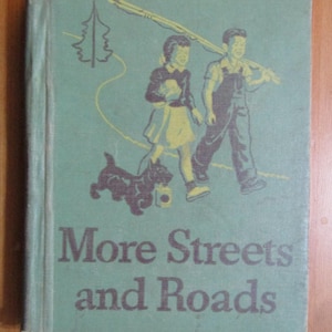 May include: Vintage book cover with the title "More Streets and Roads." The cover is a faded teal color with illustrations of two children walking with a dog. The text is in a dark brown color.