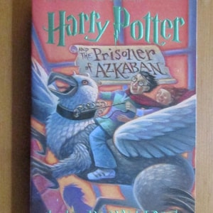 May include: A hardcover book titled "Harry Potter and the Prisoner of Azkaban" by J.K. Rowling. The cover features an illustration of Harry Potter and friends riding a Hippogriff. The Scholastic logo is visible.