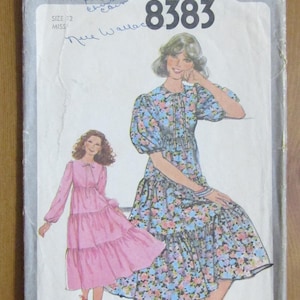 May include: Simplicity 8383 sewing pattern showing illustrations of two dresses. One dress is pink, the other is blue with a floral pattern. The pattern is size 12, Miss.