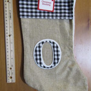 May include: A burlap Christmas stocking with a black and white checkered cuff and the letter "O". The stocking has a white trim and a red tag that reads "Holiday Style Christmas Stocking".
