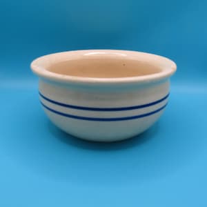 以下が含まれることがあります： 黒い持ち手と「But First, Coffee」のテキストが黒い太字で書かれた白いセラミックマグ。マグカップはぼやけた背景に置かれています。マグカップの高さは約10cmです。