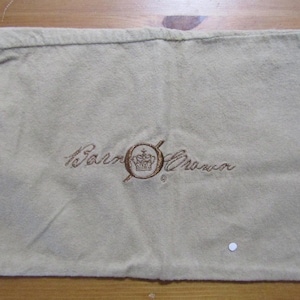 Puede incluir: Una bolsa de polvo beige con un logotipo bordado en marrón que dice "Barneys New York".