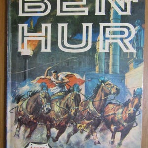 Może przedstawiać: Okładka starej książki w miękkiej oprawie z tytułem "BEN HUR" w dużych białych literach. Okładka przedstawia dramatyczną ilustrację wyścigu rydwanów z czterema końmi i woźnicą w czerwono-białej szacie. Tekst "A GOLDEN READING ADVENTURE" znajduje się w złotym ośmiokącie na dole okładki.