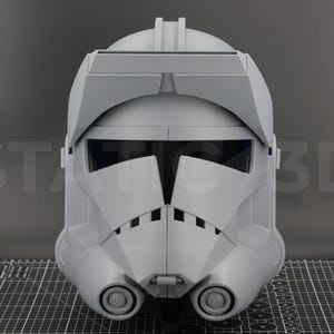 May include: A gray, detailed helmet with a visor and two circular features on the lower front. The helmet has a distinctive design, possibly for cosplay or display. The background has the text "ST 3D".