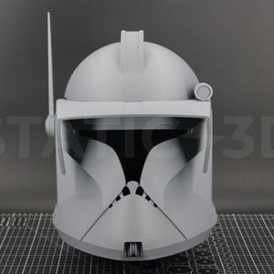 May include: A gray, 3D-printed helmet with a visor, antenna, and various details. The helmet is a replica of a Clone Trooper helmet. The text "ST 3D" is visible on the left side of the image.