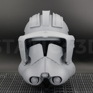 May include: A gray, 3D-printed helmet, likely for cosplay or display. The helmet features a visor, cheek pieces, and a top ridge. The design is detailed and appears to be based on a science fiction theme. The text "STAR 3D" is visible in the background.